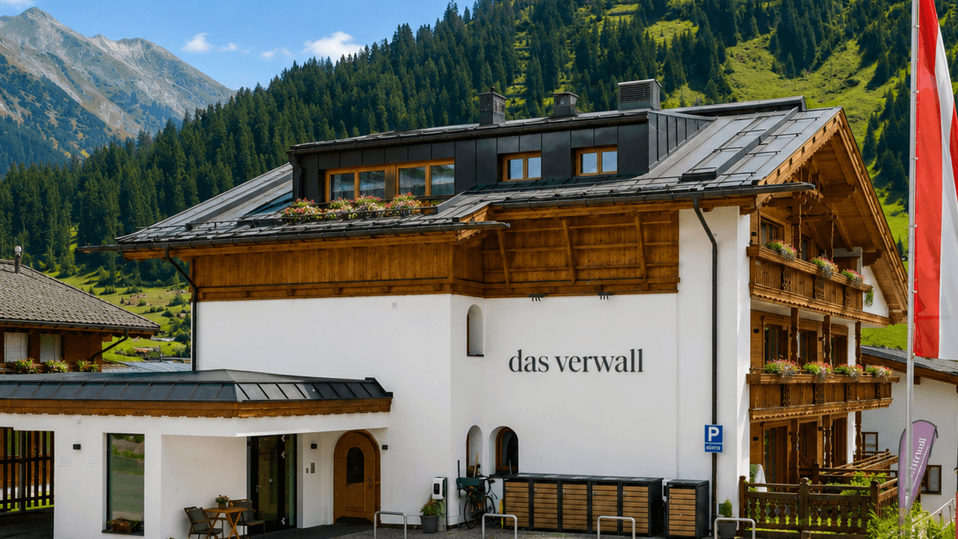 Das Verwall: Spa und Apartment in Lech am Arlberg Alphütte und Hotel in den Alpen vor bewaldeten Bergen und blauem Himmel